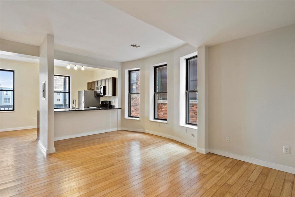 an empty living room with hardwood floors and a kitchen in the background