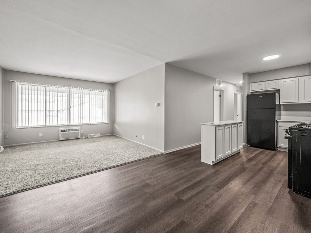 an empty living room with a kitchen in the background