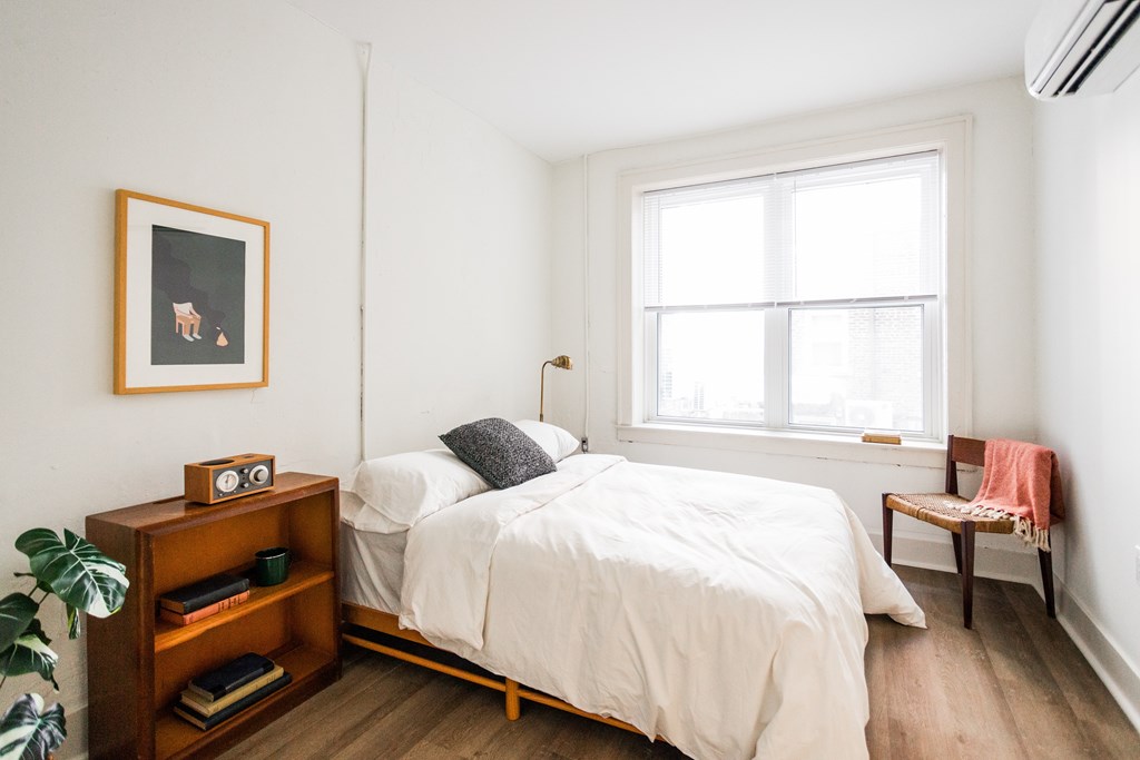 A bedroom with a bed, nightstand, and a window.