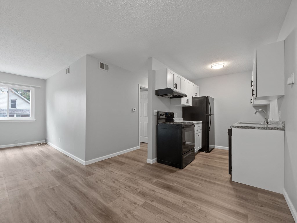 the living room and kitchen of an apartment with white walls and wood flooring