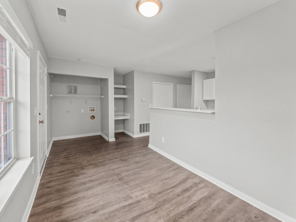 the living room and kitchen of an apartment with white walls and wood flooring