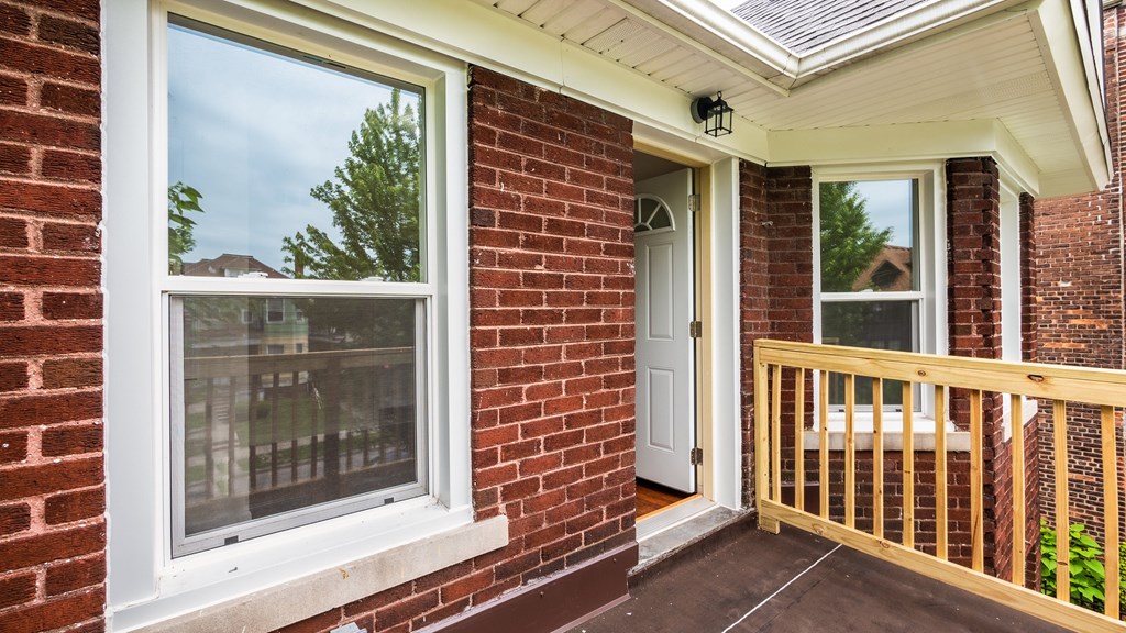 A white window on a brick house with a wooden railing.