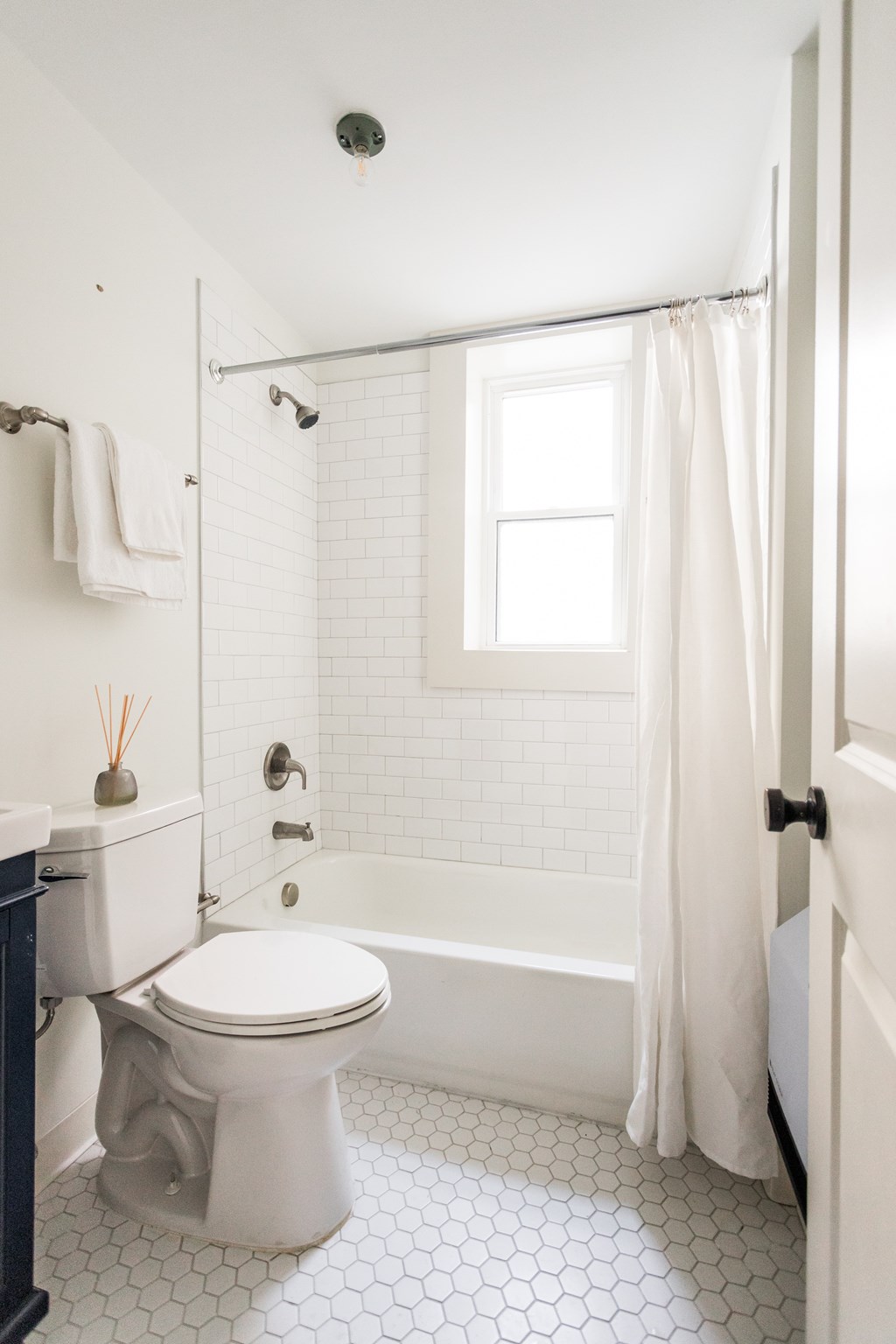 A white toilet in a bathroom with a white tiled floor and a white shower curtain.