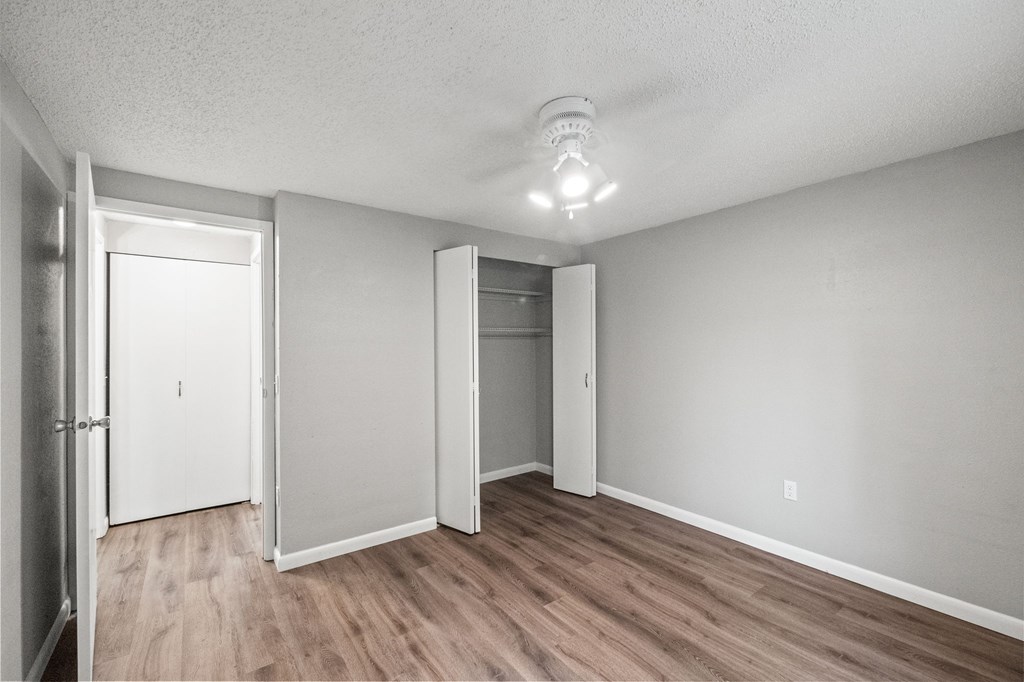 A room with a white ceiling, wooden floors, and white walls with a smoke detector on the ceiling.