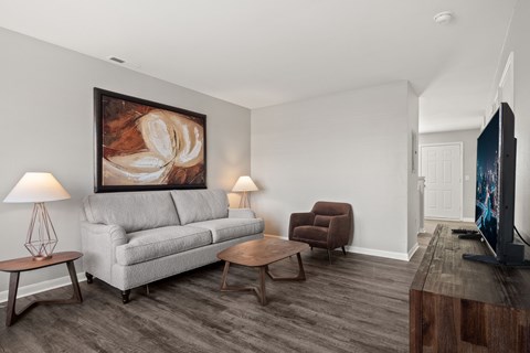 A living room with a grey couch, a brown armchair, a wooden coffee table, and a painting on the wall.