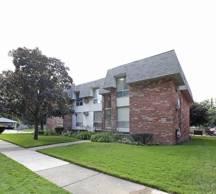 an apartment building with a green lawn and a sidewalk