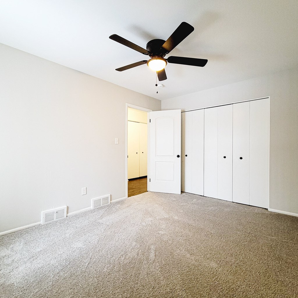 an empty living room with a ceiling fan and white closets