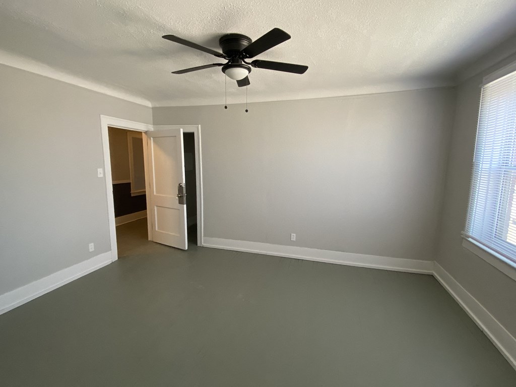an empty living room with a ceiling fan and a door to a bedroom