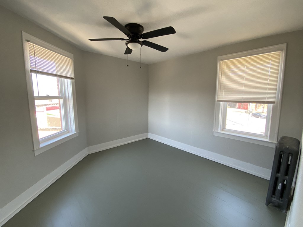 an empty room with a ceiling fan and two windows