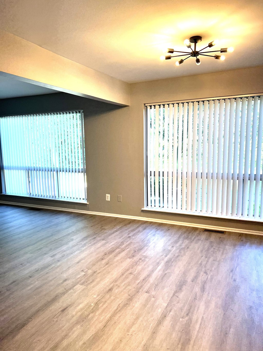 an empty living room with two windows and a chandelier