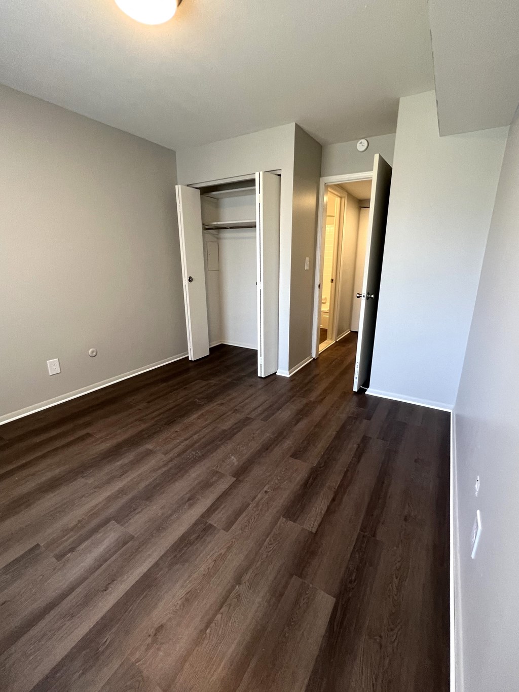an empty living room with wood flooring and a hallway with a closet