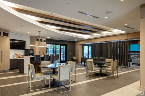 a lounge area with tables and chairs and a kitchen and a television