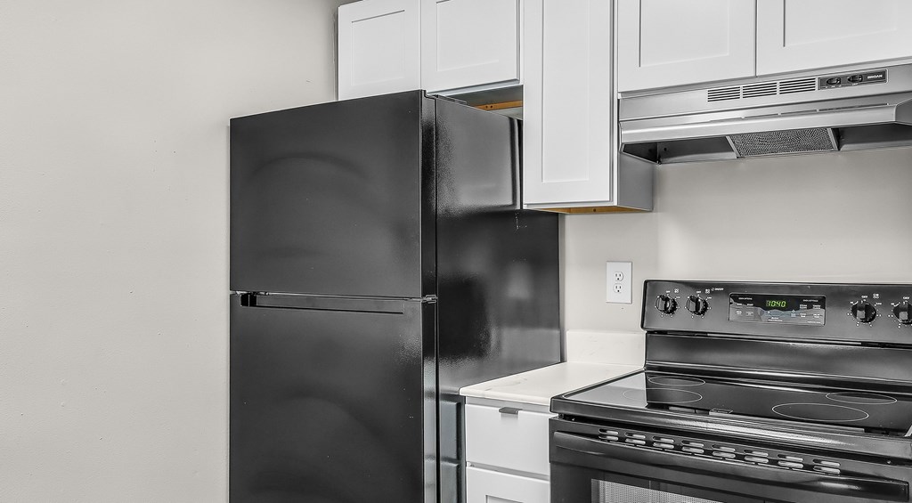 A black refrigerator is in a kitchen with white cabinets.