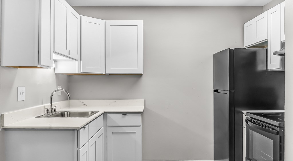 A kitchen with white cabinets and a black refrigerator.
