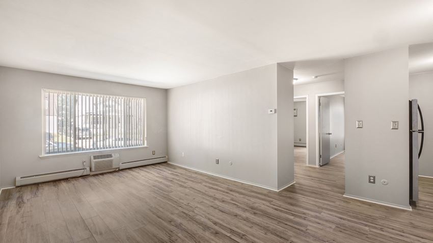 the living room and hallway of an apartment with wood flooring and a window