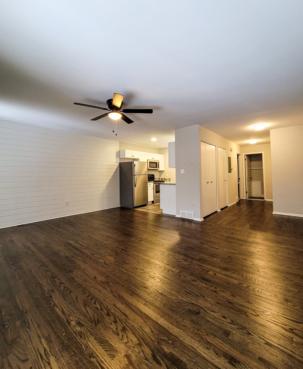 an empty living room with a ceiling fan and a kitchen