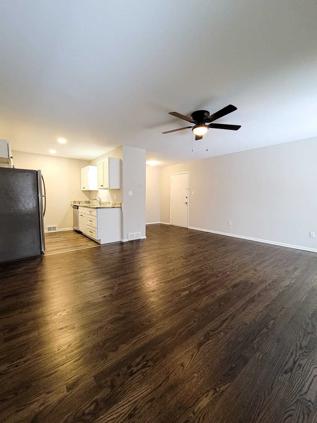 an empty living room with a ceiling fan and a kitchen