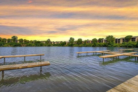 A serene lake with wooden benches and a building in the distance under a twilight sky.
