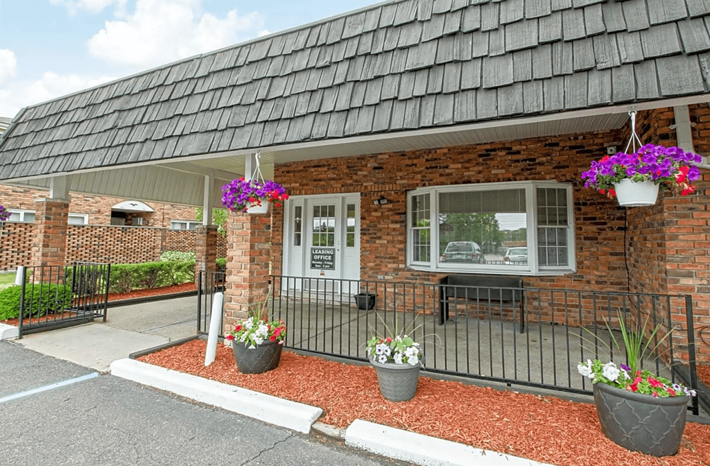 the front of a brick building with a porch and flowers in pots