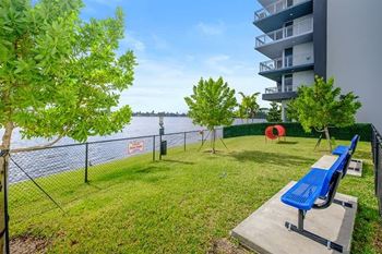 A blue bench sits on a concrete slab in a grassy area next to a fence.