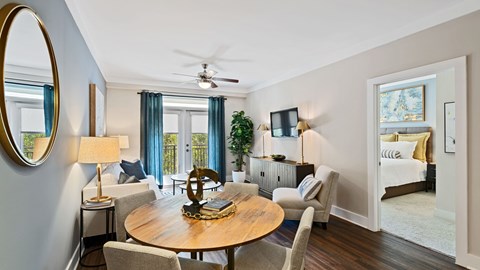 A living room with a round wooden table and chairs, a mirror, and a ceiling fan.