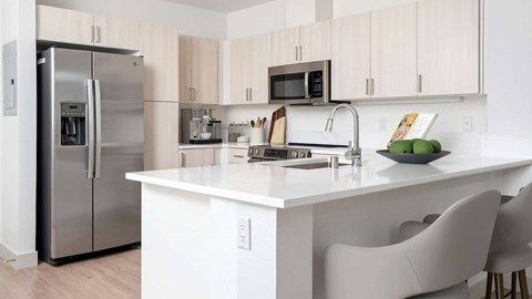 A kitchen with a refrigerator, microwave, and white countertop.
