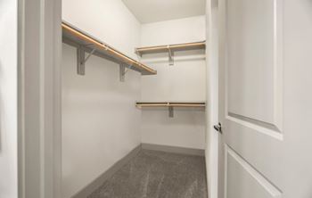 A white door is open to a small, empty room with a grey carpet and two shelves.