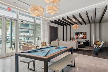A pool table is in the middle of a room with a bench and a chair.