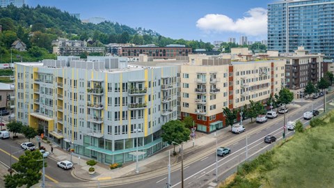 A multi-story building with a mix of yellow, white, and red colors sits next to a busy street with cars and a pedestrian crossing.