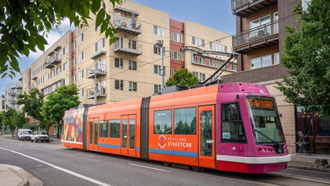 A streetcar with a pink and orange design is on a street.