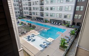 A large swimming pool with lounge chairs and umbrellas is surrounded by apartment buildings.