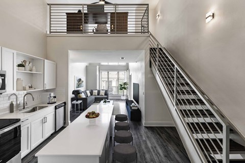 a kitchen and living room with a staircase in the background