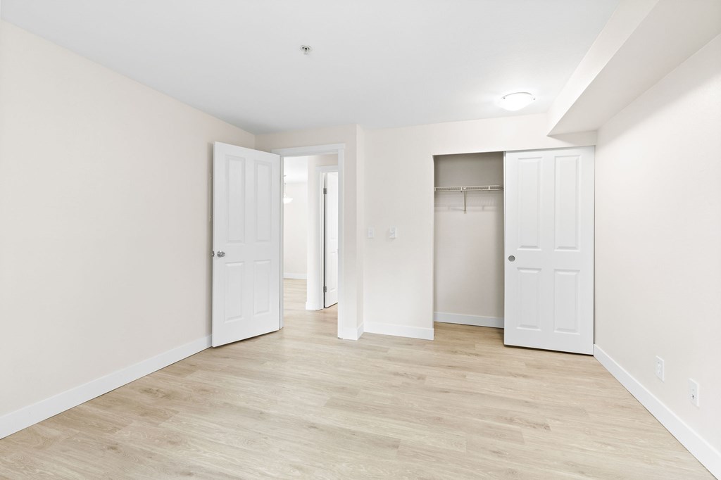 A room with white walls and wooden flooring with two white doors.