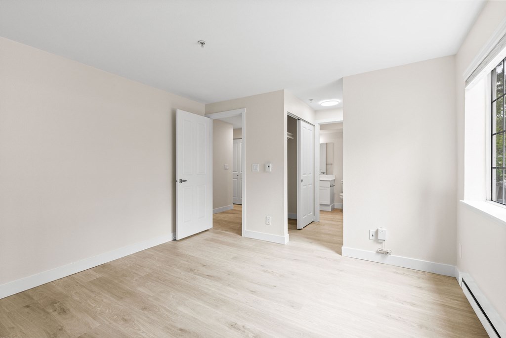A room with white walls and wooden flooring with a doorway leading to another room.