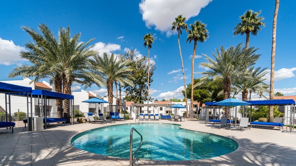 a swimming pool with blue umbrellas and palm trees in the background