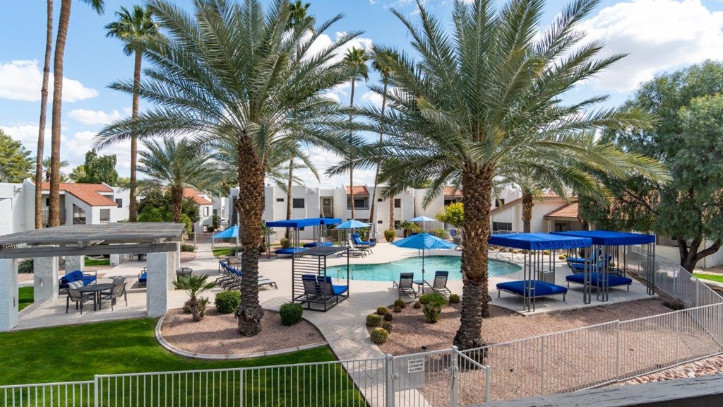 A pool surrounded by palm trees and blue umbrellas.