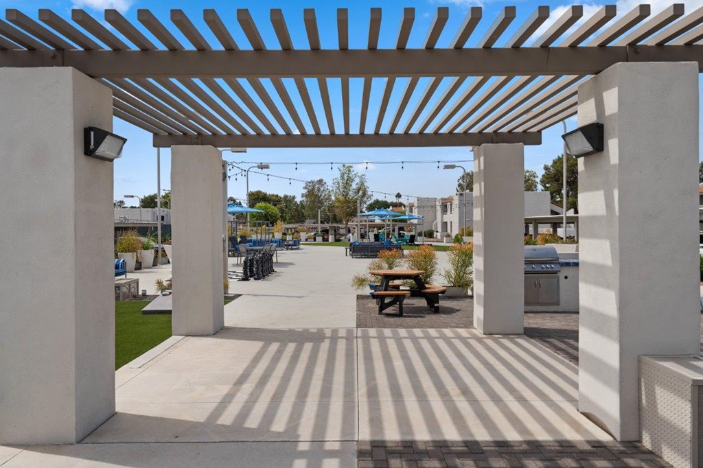 A white pergola with a striped floor and a picnic table underneath.