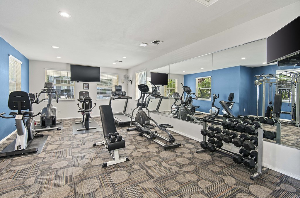 a gym with weights and cardio equipment in a room with mirrored walls