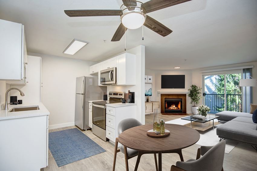 a kitchen and living room with a ceiling fan and a fire in the fireplace - Photo Gallery 1