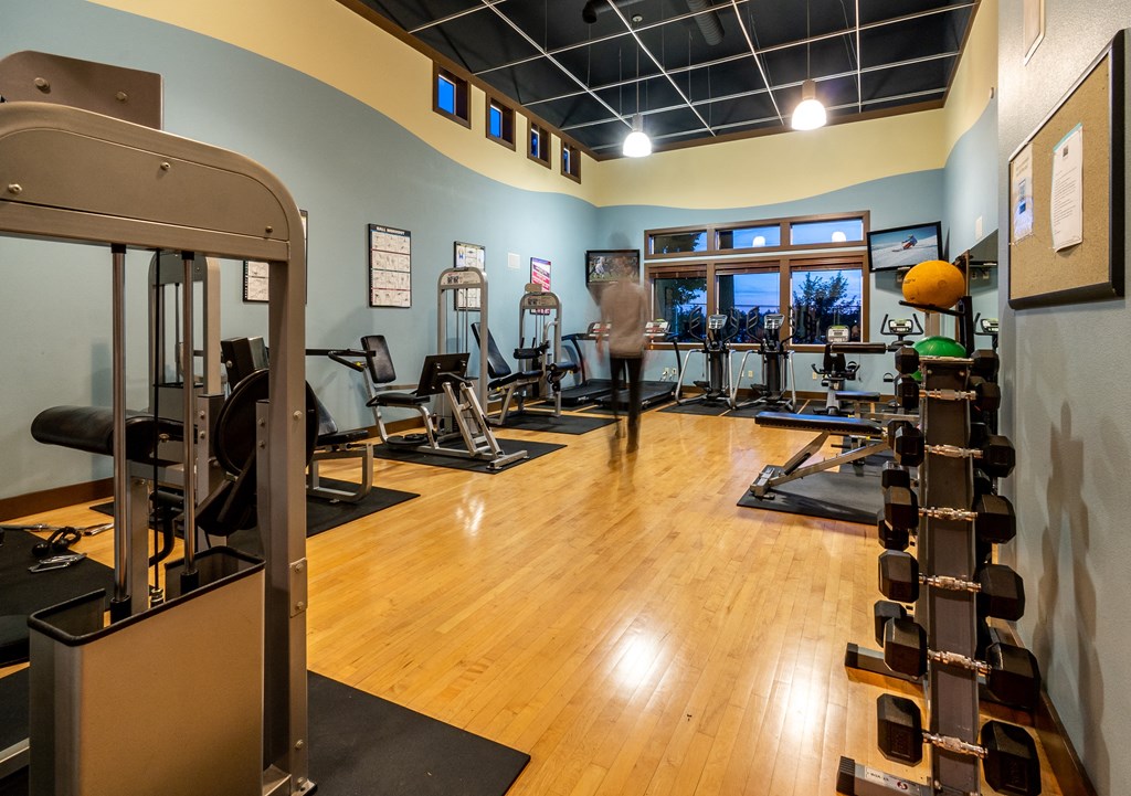 a spacious fitness room with cardio equipment and a man working out in the background
