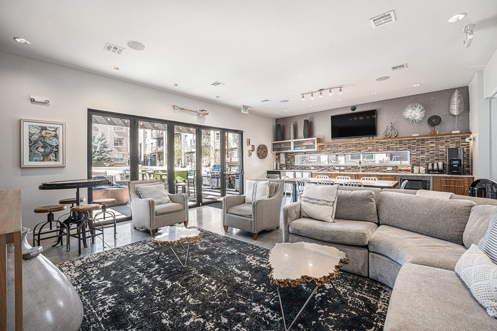 A modern living room with a black and white rug, a grey sofa, and a flat screen TV mounted on the wall.