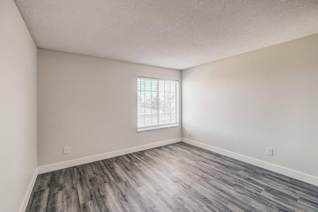 an empty bedroom with hardwood floors and a window