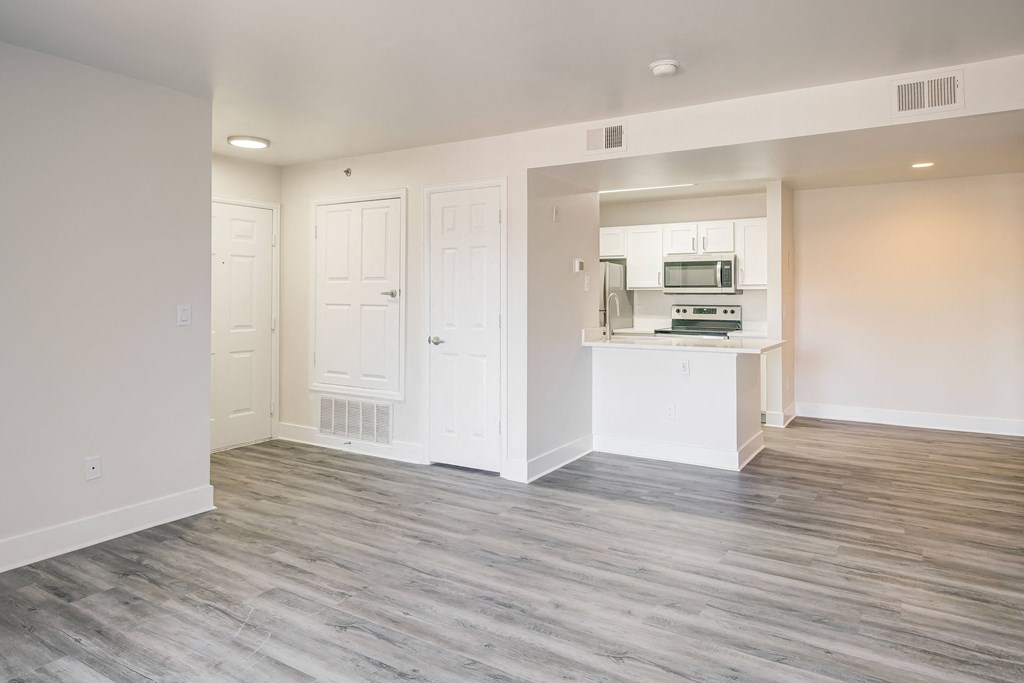 an empty living room with a kitchen in the background