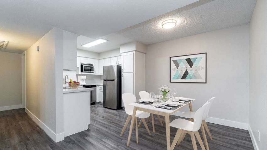a dining area with a table and chairs and a kitchen in the background - Photo Gallery