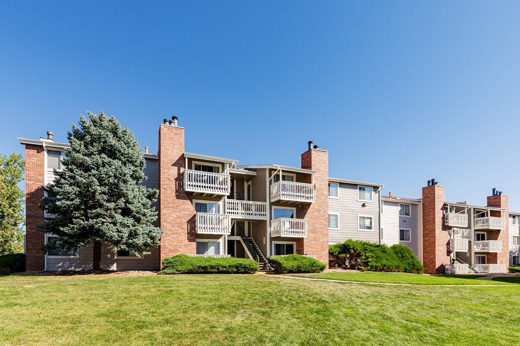 an exterior view of an apartment building with green grass and a tree