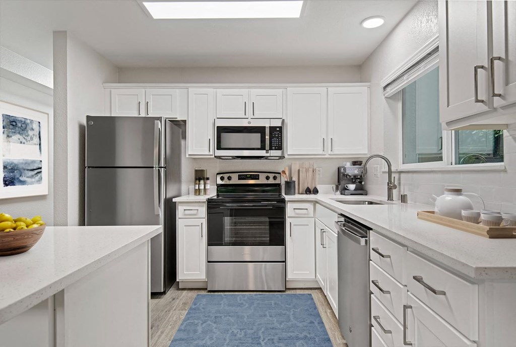 a white kitchen with stainless steel appliances and a blue rug