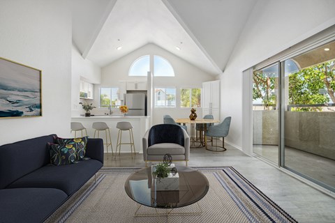 a living room with a couch and a coffee table in front of a kitchen with a breakfast