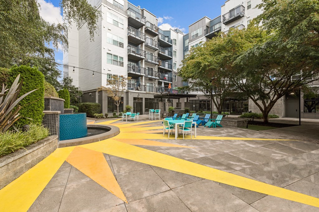 a courtyard with a yellow arrow painted on the ground and turquoise chairs and tables