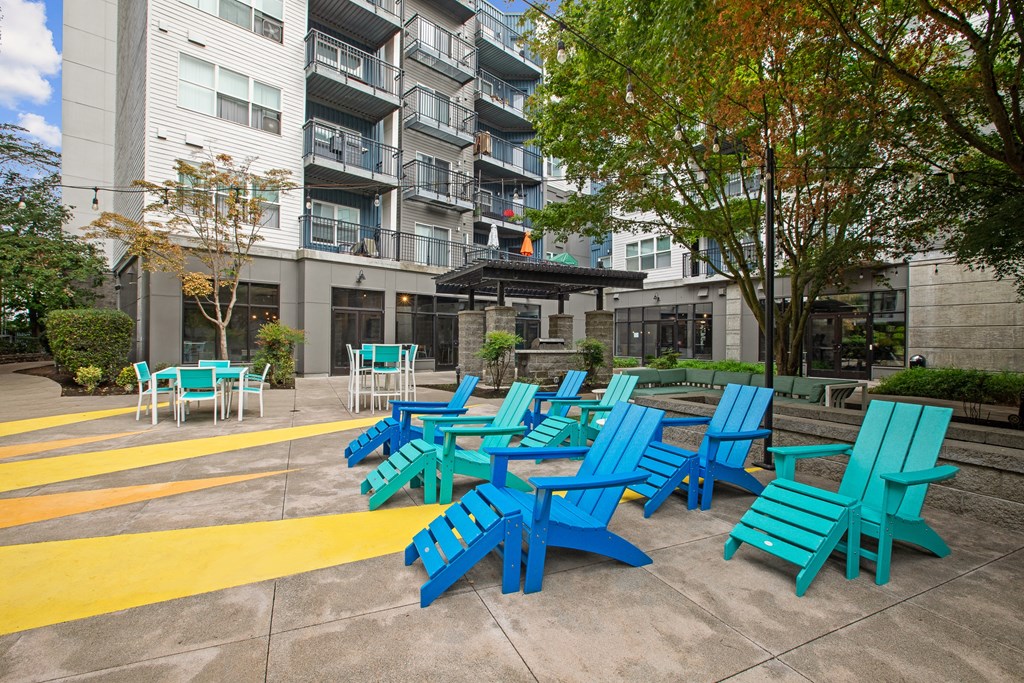 an outdoor lounge area with blue and green chairs and a yellow and white building in the background
