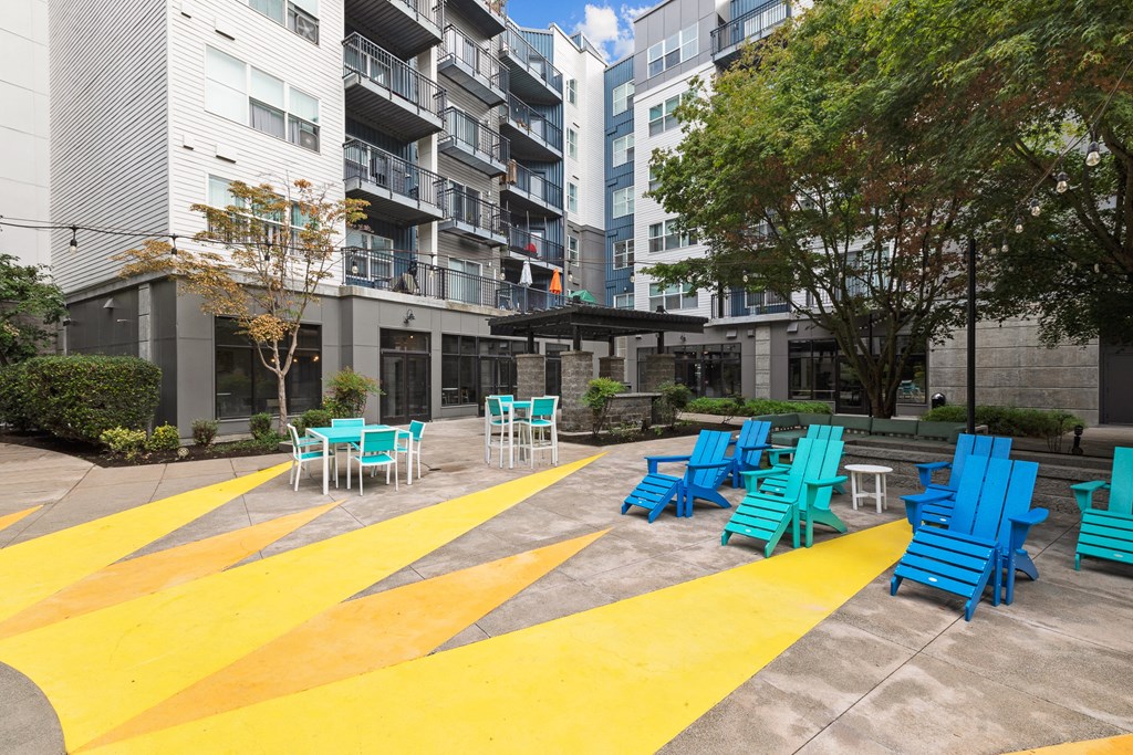 an outdoor seating area with blue chairs and tables on a sidewalk in front of an apartment building